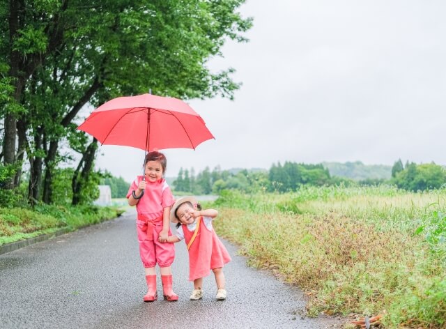 ピンク色の傘をさしポーズをとる子供たちの写真